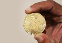 Foto asli seseorang memegang koin fisik Bitcoin sebagai ilustrasi aset kripto