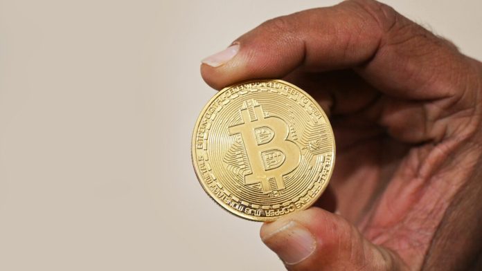 Foto asli seseorang memegang koin fisik Bitcoin sebagai ilustrasi aset kripto